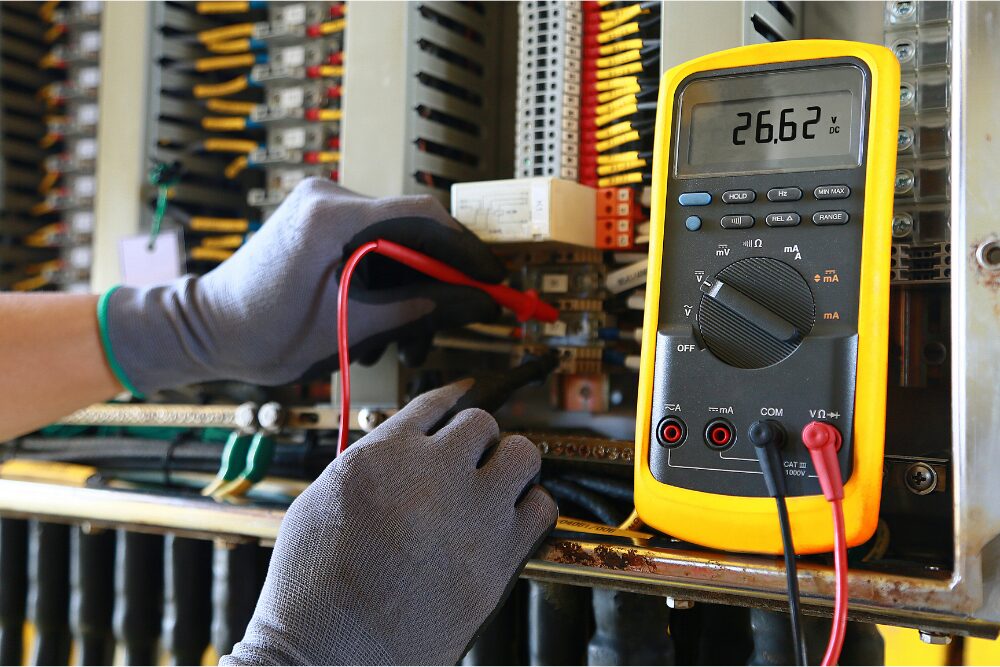 Kelvin Electric technician using a digital multimeter to test voltage inside a commercial electrical panel in Oklahoma City.